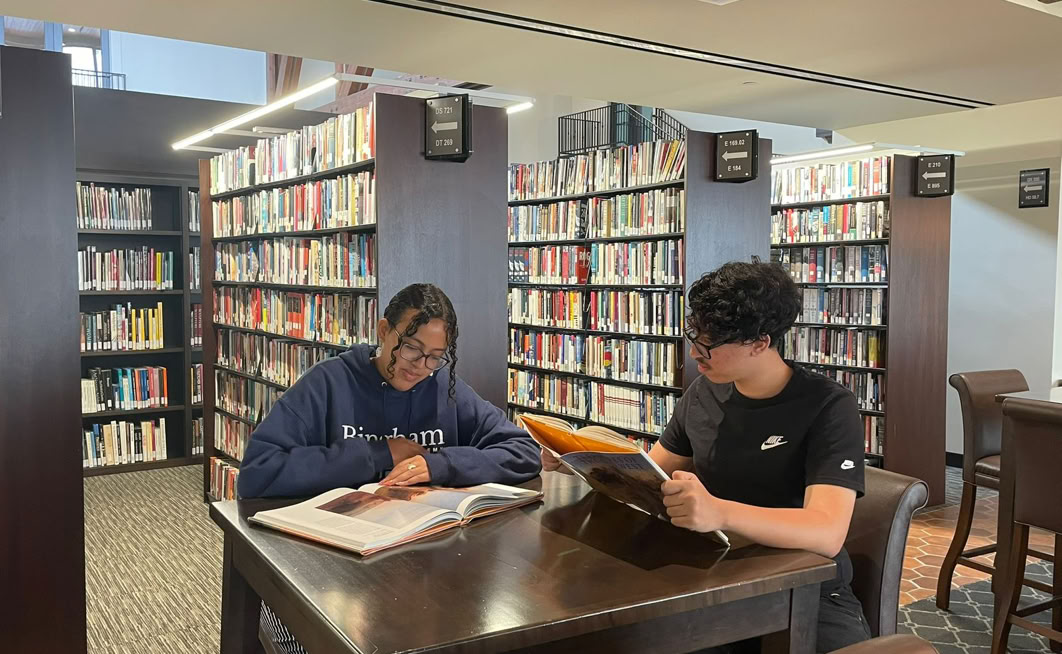 Two people studying at a table in an-nour university library surrounded by bookshelves.